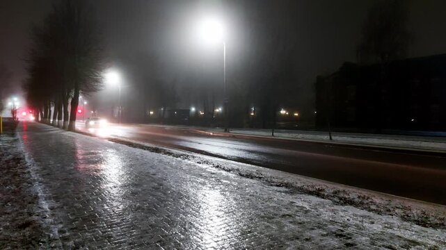 Ice on the sidewalk against the background of the road with car headlights at night in winter, slippery road, ice-crusted ground
