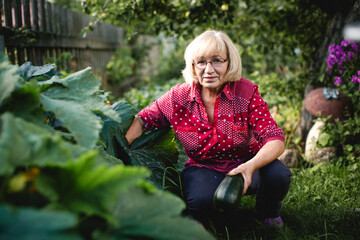 A middle-aged woman stands in her garden holding a zucchini, surrounded by greenery. The scene...