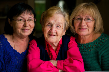 A touching portrait of an elderly woman with her two middle-aged daughters. Their faces reflect...