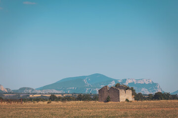 Ancient stone ruins stand alone in a vast field amid rolling hills under a clear blue sky in the countryside