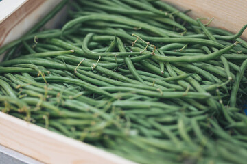 Fresh green beans displayed in a wooden box at a local market during daylight hours