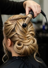 Fototapeta premium Hairstylist Creating Elegant Updo Hairstyle on Blonde Woman Using Curling Iron