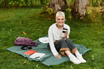 Stylish young woman enjoys a relaxing afternoon in the park with coffee and a book