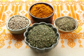 Many different aromatic spices in bowls on table with cloth, closeup