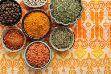 Many different aromatic spices in bowls on table with cloth, flat lay. Space for text