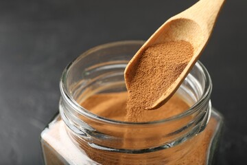 Adding instant coffee powder from spoon into jar on dark table, closeup