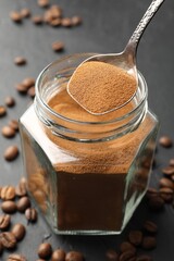 Taking instant coffee powder from jar with spoon at dark table, closeup