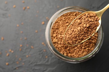 Spoon with granulated instant coffee and jar on dark textured table, top view. Space for text