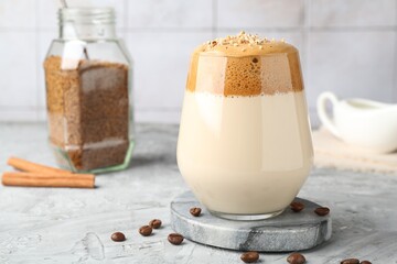 Delicious dalgona coffee in glass, beans, granules and cinnamon on grey table, closeup