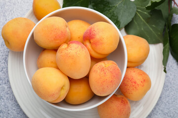 Fresh apricots in bowl and green leaves on grey textured table, flat lay