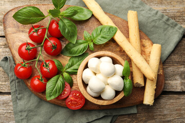 Tasty mozzarella cheese balls, tomatoes, basil and grissini on wooden table, top view