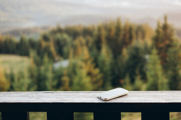 Smartphone on wooden railing with blurred forest background in morning light.
