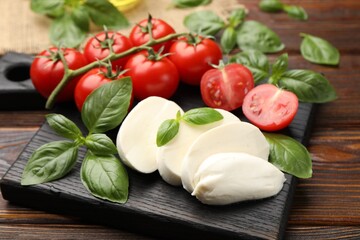Tasty mozzarella cheese, tomatoes and basil on wooden table, closeup