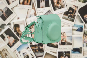 Turquoise Polaroid camera with leather case on background with polaroid images