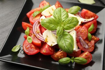 Tasty salad Caprese with mozzarella, tomatoes, basil, onion and spices on table, closeup