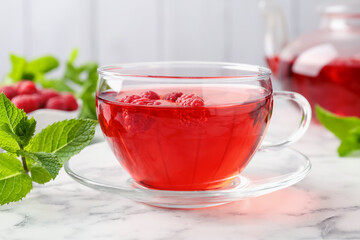 Tasty raspberry tea, berries and leaves on white marble table, closeup