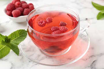 Tasty raspberry tea, berries and leaves on white marble table, closeup