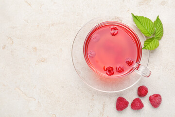 Tasty raspberry tea in glass cup, berries and green leaves on light grey table, flat lay. Space for...