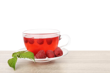 Tasty raspberry tea in glass cup, berries and green leaves on wooden table against white background
