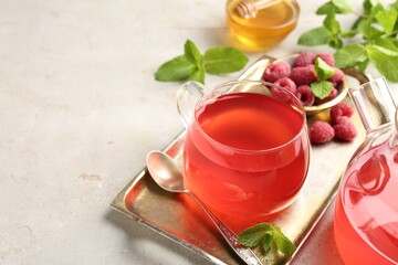 Tasty raspberry tea, teapot, berries, honey and mint on light grey table, closeup. Space for text