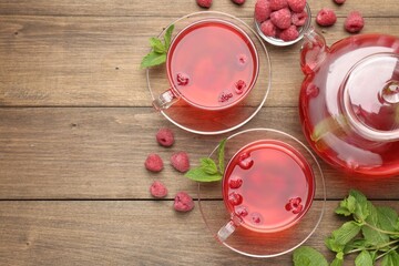 Tasty raspberry tea in glass cups, teapot, berries and mint on wooden table, flat lay. Space for text