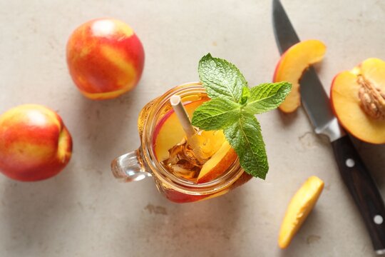 Refreshing iced peach tea with mint in mason jar and fresh fruits on light table, flat lay