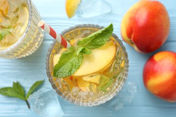 Tasty iced tea with peaches and mint on light blue wooden table, flat lay