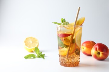 Fototapeta premium Tasty iced tea with lemon, peaches and mint on white background