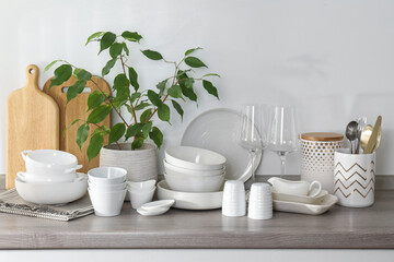 Different clean white dishware, wooden cutting boards, glasses, cutlery and houseplant on counter in kitchen