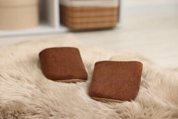 Stylish brown slippers on fluffy carpet indoors, closeup