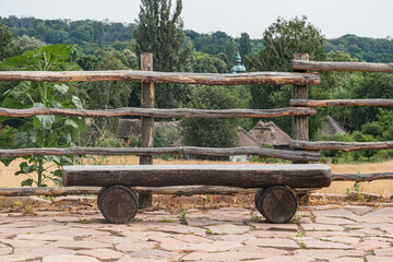 Ancient European village Weathered wooden bench with wheels on cobblestone path, rural backdrop of...