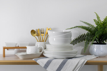 Different clean white dishware and cutlery on wooden table indoors