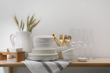 Different clean white dishware, glasses, cutlery and spikes on wooden table indoors