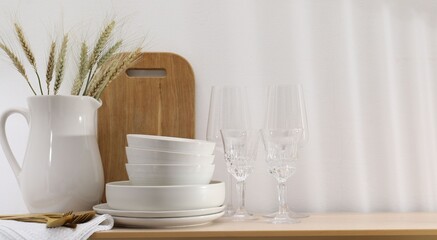 Different clean white dishware, cutlery, cutting board, glasses and spikes on wooden table indoors, space for text
