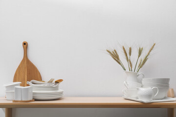 Different clean white dishware, cutting board and spikes on wooden table indoors