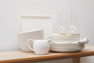 Different clean white dishware and glasses on wooden table indoors