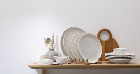 Clean dishware and cutting board on wooden table near white wall. Space for text