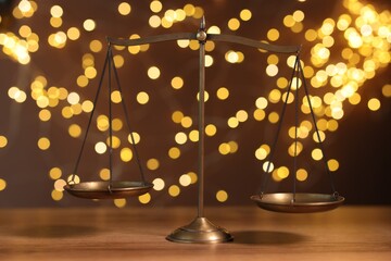 Golden scales of justice on wooden table against blurred lights
