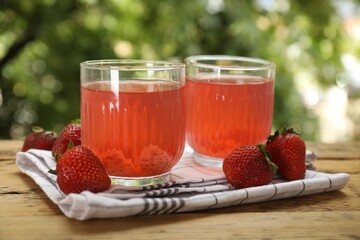 Tasty compot in glasses and fresh strawberries on wooden table outdoors, closeup
