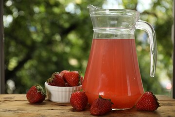 Tasty compot in glass jug and fresh strawberries on wooden table outdoors, closeup