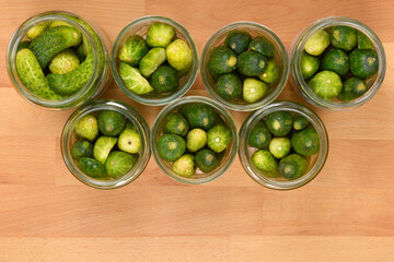 Several open glass jars filled with fresh cucumbers, arranged on a wooden surface and ready for pickling or preserving