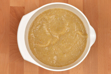 A white plastic bowl filled with cooked mashed apples, ready for apple pie, placed on a wooden surface
