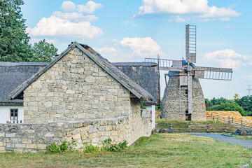 Stone windmill in open field, multi-story structure with wooden wheel, thatched roof, small trees...