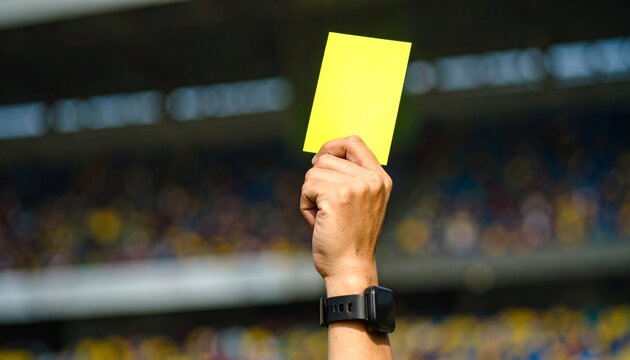 Referee holding up yellow card during soccer match in stadium warning player