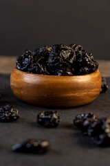 old bowl filled with dried black prunes made from small plums, dark-colored dried plum fruits poured into a wooden bowl, closeup