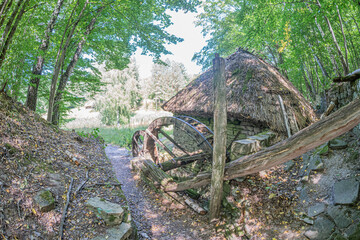 Old wooden village structure amidst a forested, leaf-covered landscape in an isolated setting,...