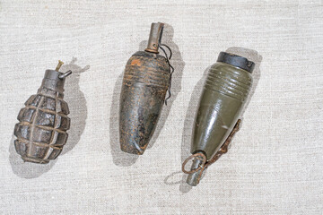 Three vintage fragmentation hand grenades displayed on a light beige, textured fabric surface...
