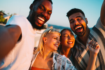 Happy friends laughing together at sunset on a rooftop party