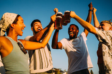 Group of cheerful multi-ethnic friends toasting with beer glasses while enjoying a sunset party