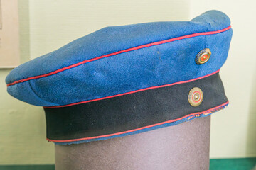 Indoors image of antique military cap, blue with red piping, featuring two insignia one with a star...